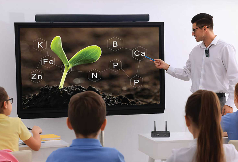 Teacher teaching in a classroom using the Wireless Teacher Mic AW315 and Soundbar GS-68C. Both devices can be seamlessly integrated into the classroom environment to maintain student engagement and ensure comprehension.